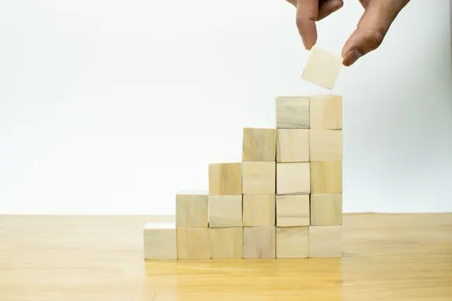 and placing a wooden block on top of a staircase-like structure made of stacked wooden cubes, symbolizing growth and progress